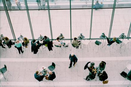 CLub entreprises.jpg Des personnes dans un hall, certaines passent, certaines sont assises à des tables